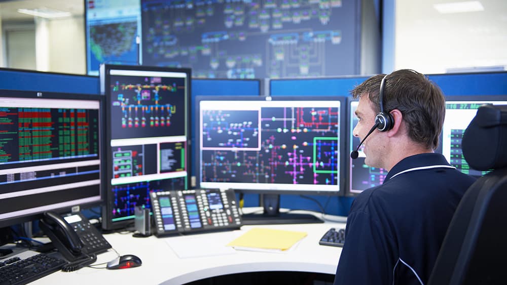 Control room operator monitoring electrical network data across multiple screens.